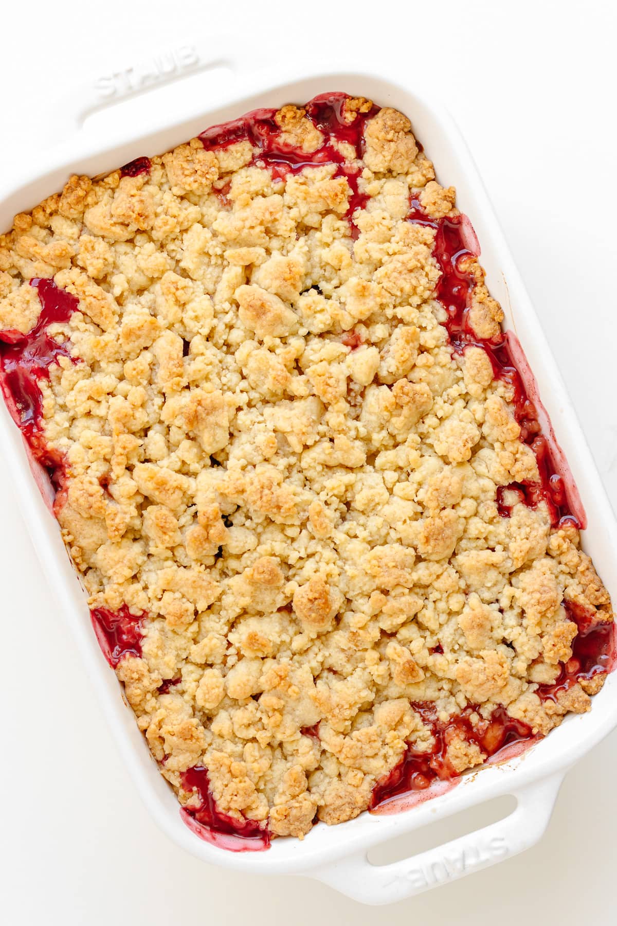 A baked plum and apple crumble in a white baking dish.