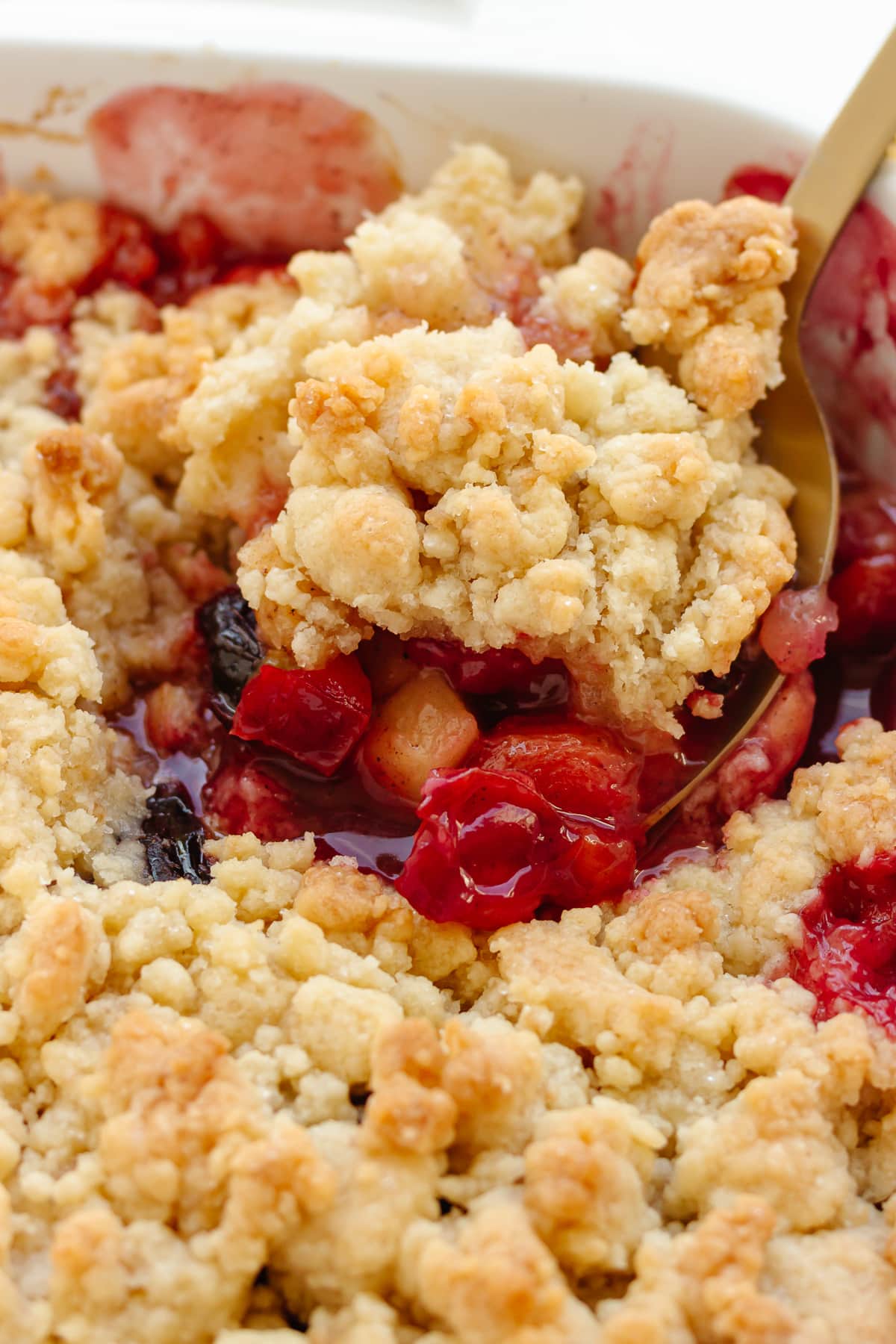 Scoop of plum and apple crumble being lifted from baking dish.