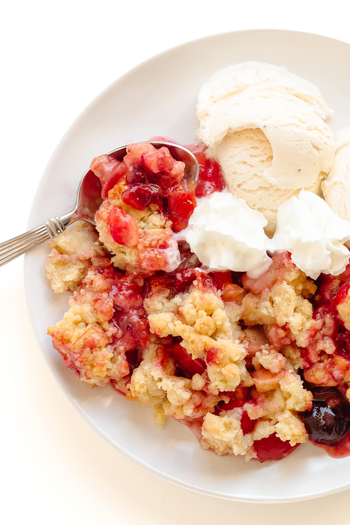 Plum and apple crumble on a plate served with vanilla ice cream and whipped cream.