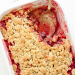Plum and apple crumble in a white baking dish with a portion scooped out.