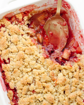Plum and apple crumble in a white baking dish with a portion scooped out.