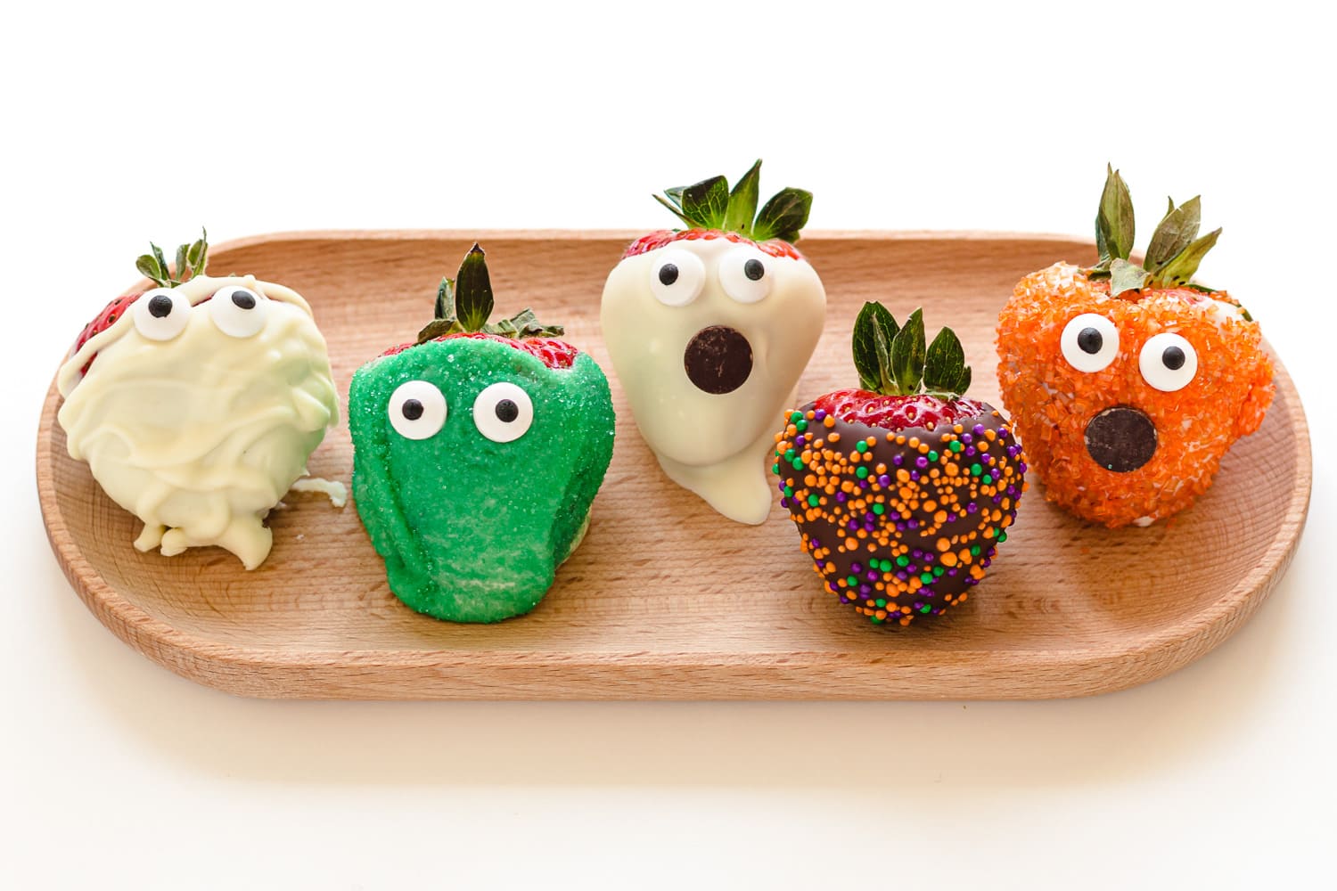 Five different decorated Halloween strawberries lined up on a wooden tray.