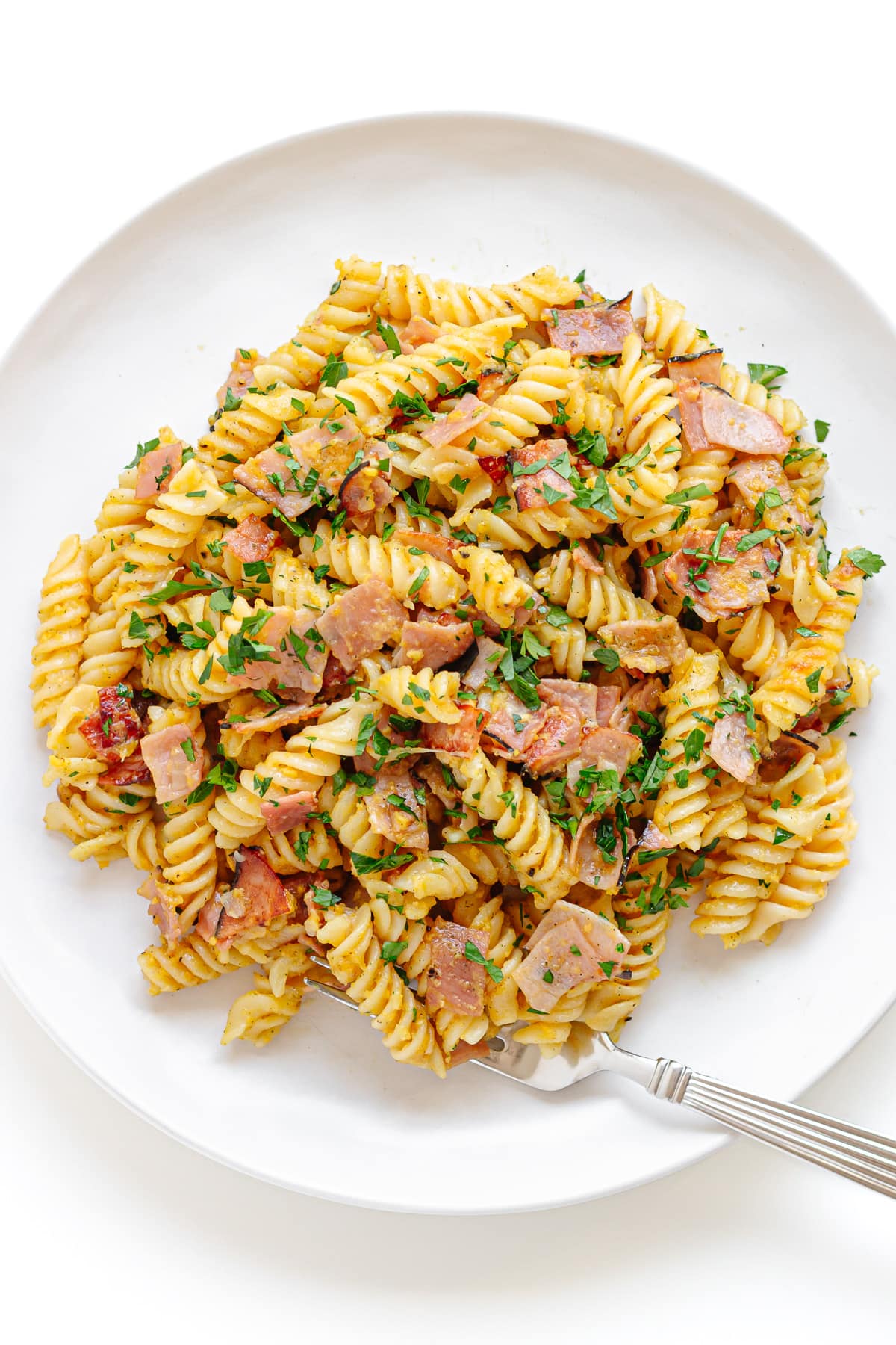 German ham and egg pasta on a white plate with a fork.