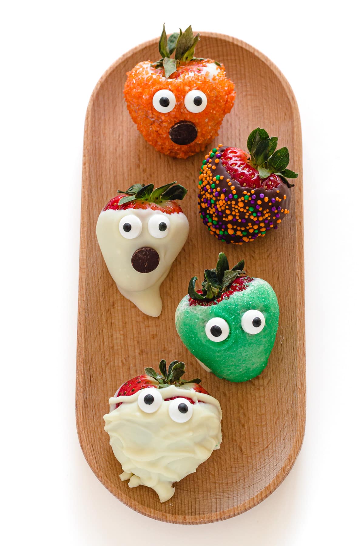 Five different types of easy Halloween chocolate strawberries lined up on a wooden tray.