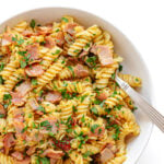 Closeup of a bowl of Schinkennudeln (German Ham and Egg Pasta) with a fork scooping out a bite.
