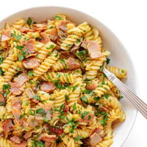 Closeup of a bowl of Schinkennudeln (German Ham and Egg Pasta) with a fork scooping out a bite.