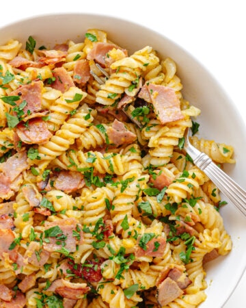 Closeup of a bowl of Schinkennudeln (German Ham and Egg Pasta) with a fork scooping out a bite.