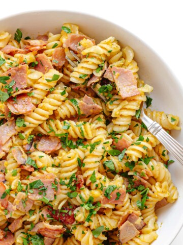 Closeup of a bowl of Schinkennudeln (German Ham and Egg Pasta) with a fork scooping out a bite.