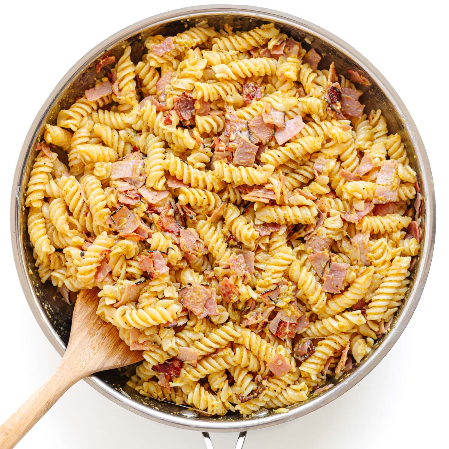 Ham and egg pasta being pan fried in a stainless steel skillet with a wooden spoon.