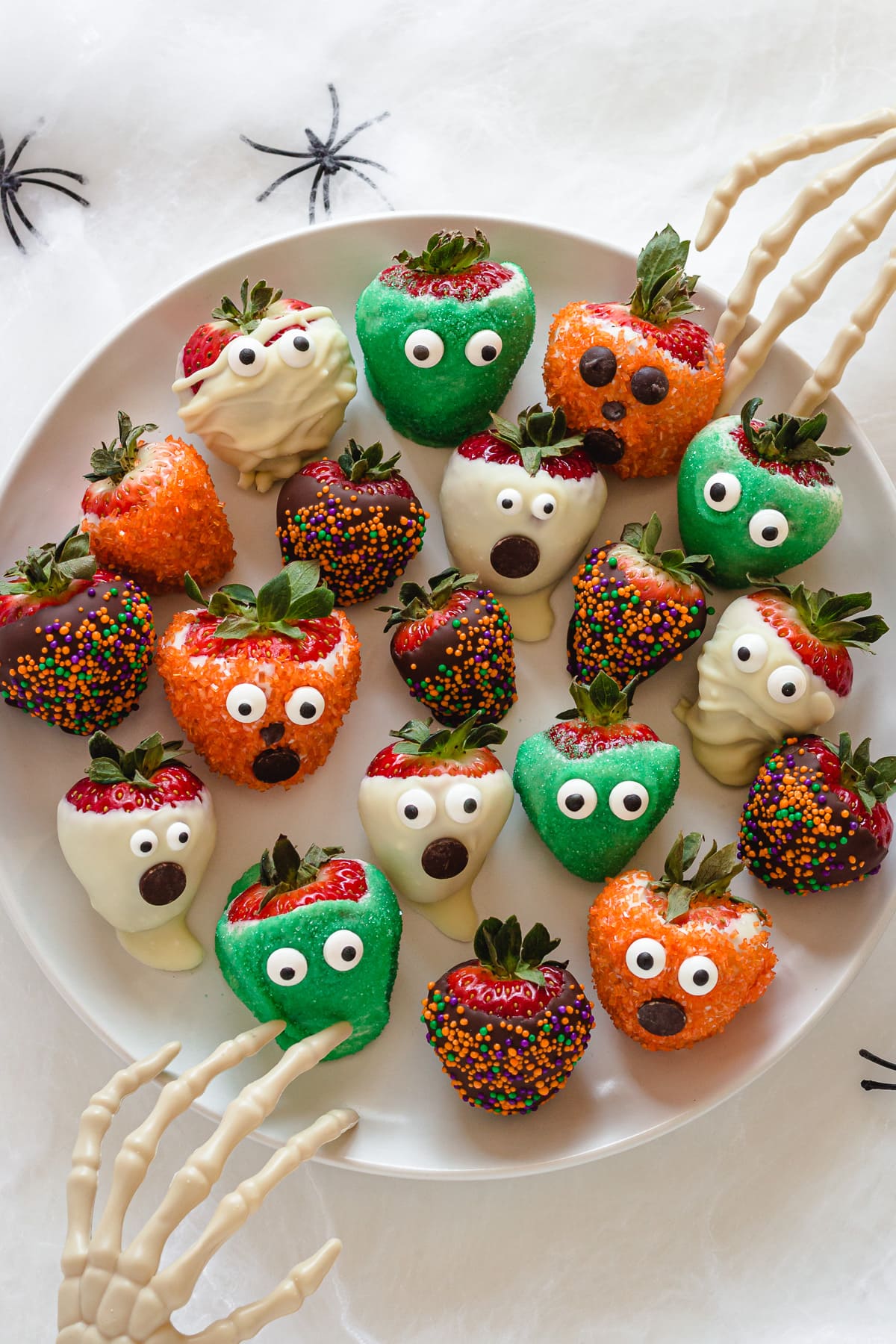 A white platter of spooky Halloween strawberries with two skeleton hands reaching in.