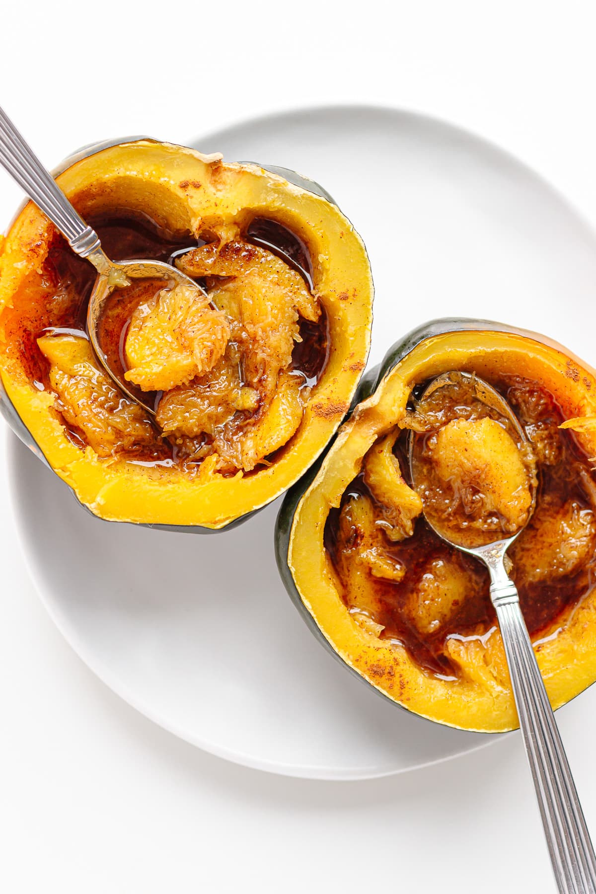 Two acorn squash halves with butter and brown sugar on a white plate with a spoons digging into each half.