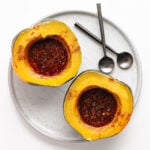 Two pressure cooked acorn squash halves filled with butter and brown sugar topping on a serving plate with two spoons.