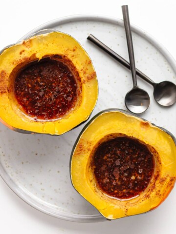 Two pressure cooked acorn squash halves filled with butter and brown sugar topping on a serving plate with two spoons.