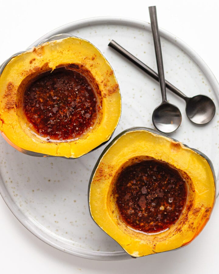 Two pressure cooked acorn squash halves filled with butter and brown sugar topping on a serving plate with two spoons.