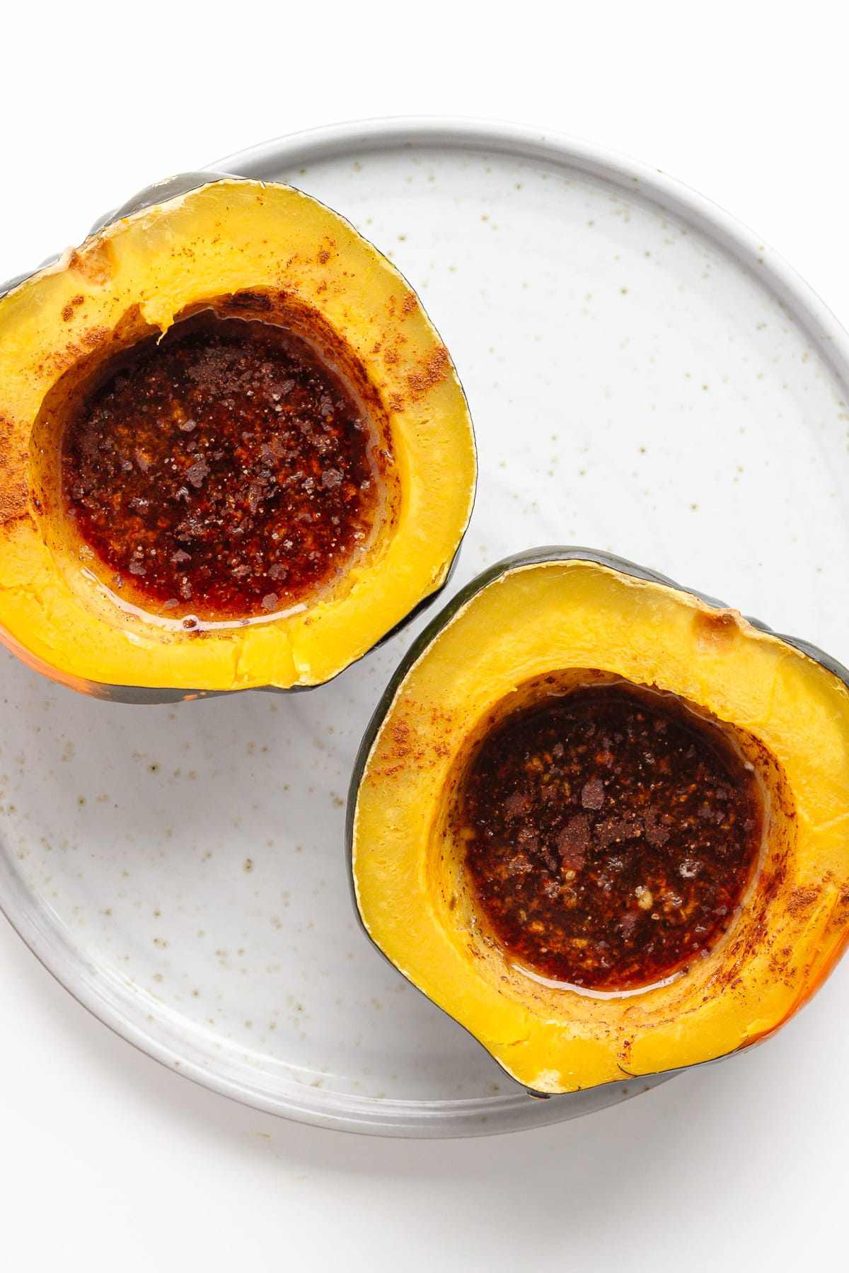 Two cooked acorn squash halves on a serving plate filled with a butter, brown sugar and cinnamon topping.