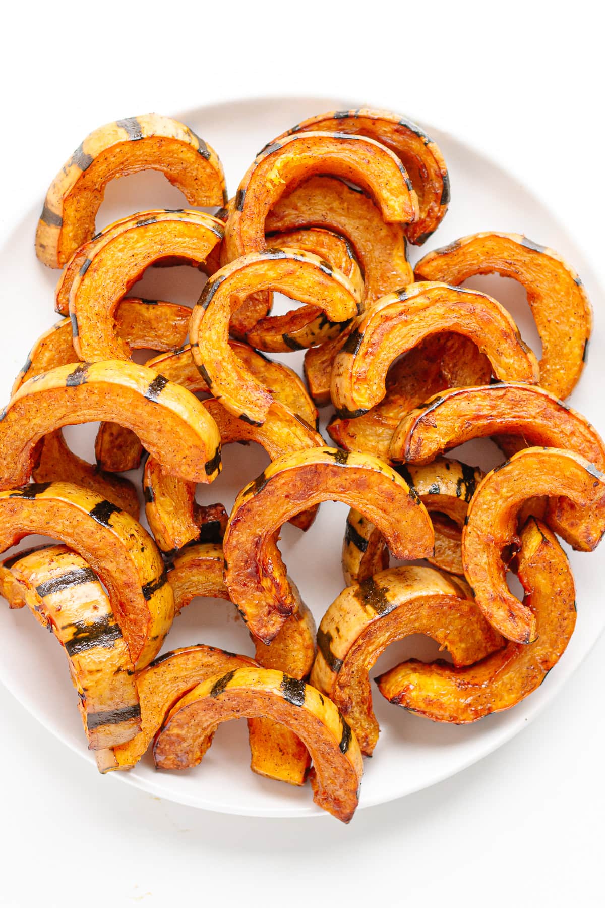 Maple roasted delicata squash slices on a white plate.