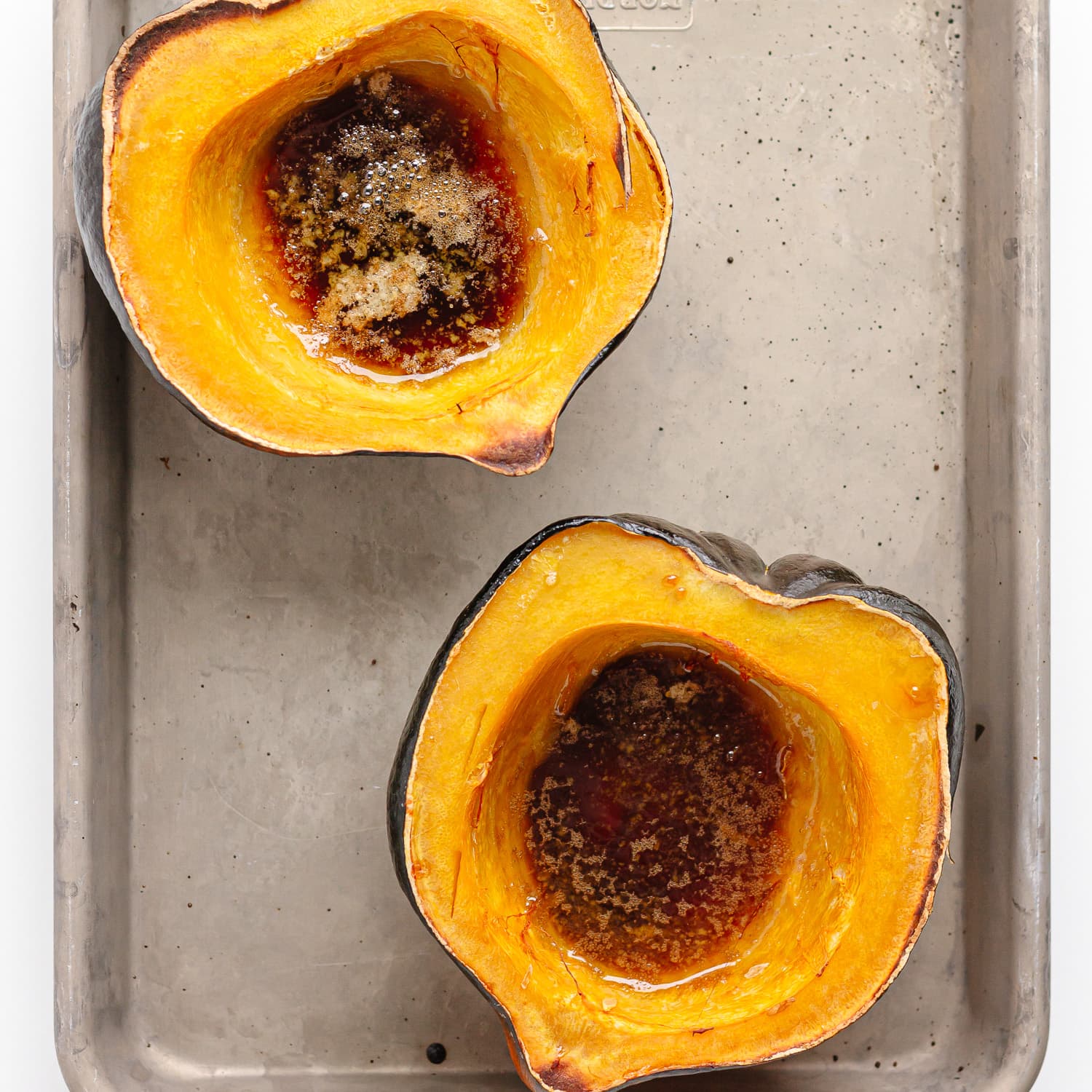 Two roasted acorn squash halves on a baking sheet with butter and brown sugar topping inside.