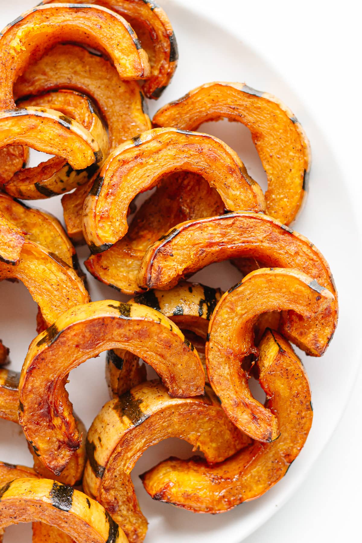Oven roasted delicata squash slices on a white plate.