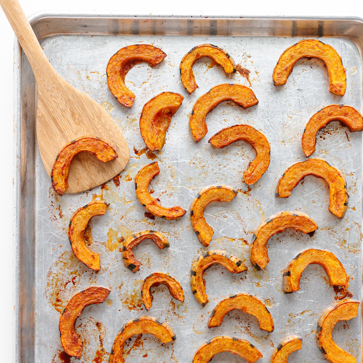 Roasted delicata squash half moon slices on a baking sheet.