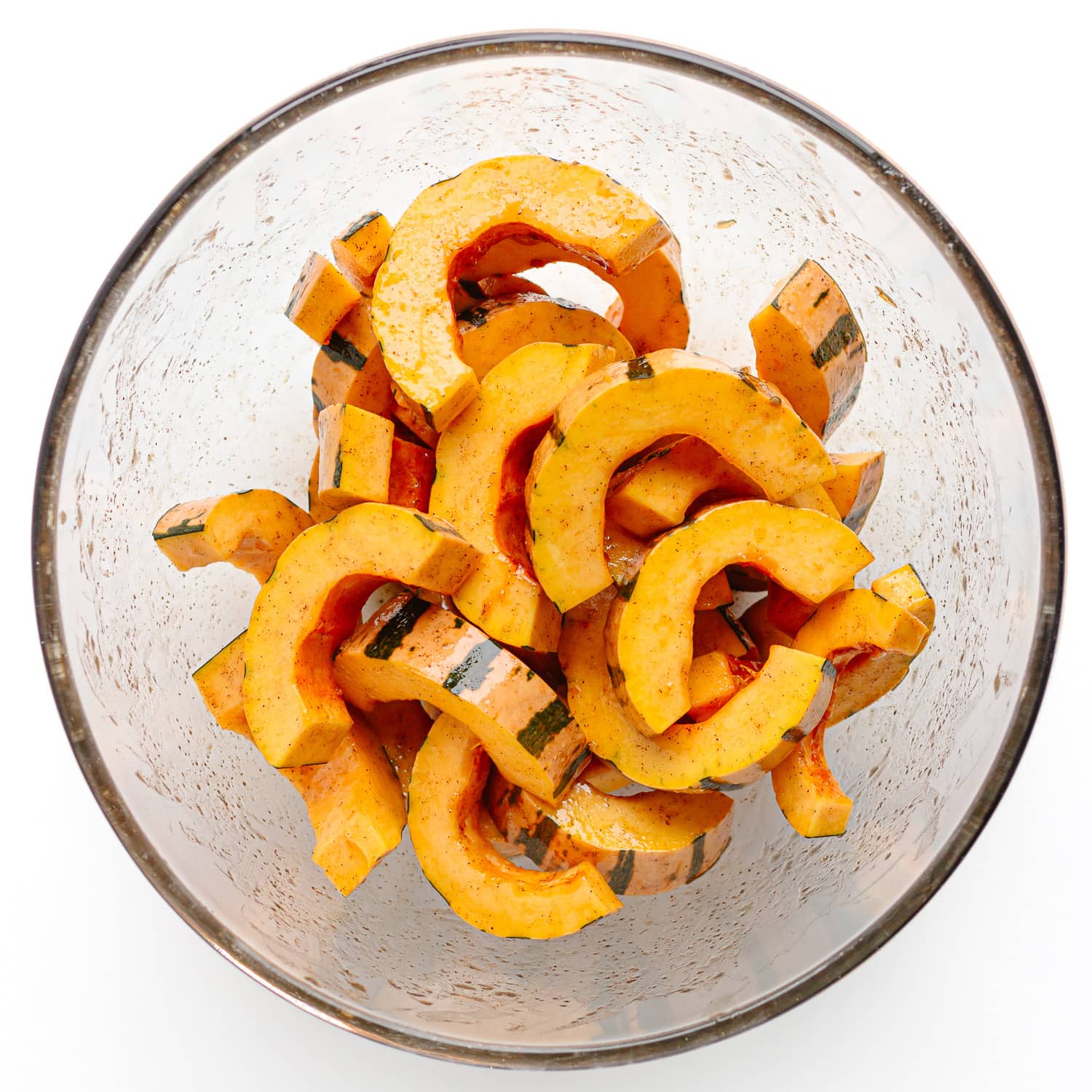 Slices of delicate squash coated in maple syrup mixture in a glass bowl.
