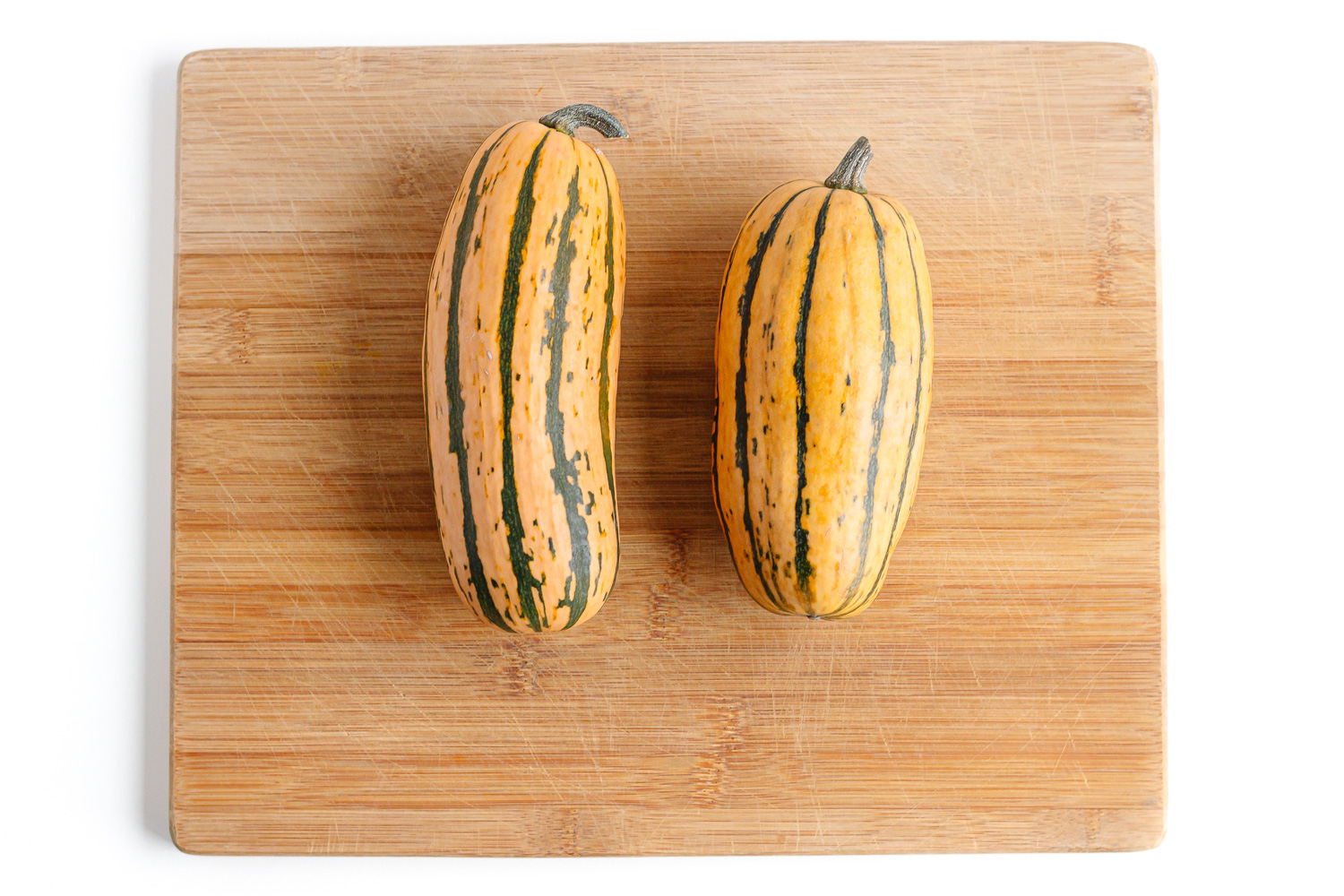 Two delicate squash sitting on a wooden cutting board.