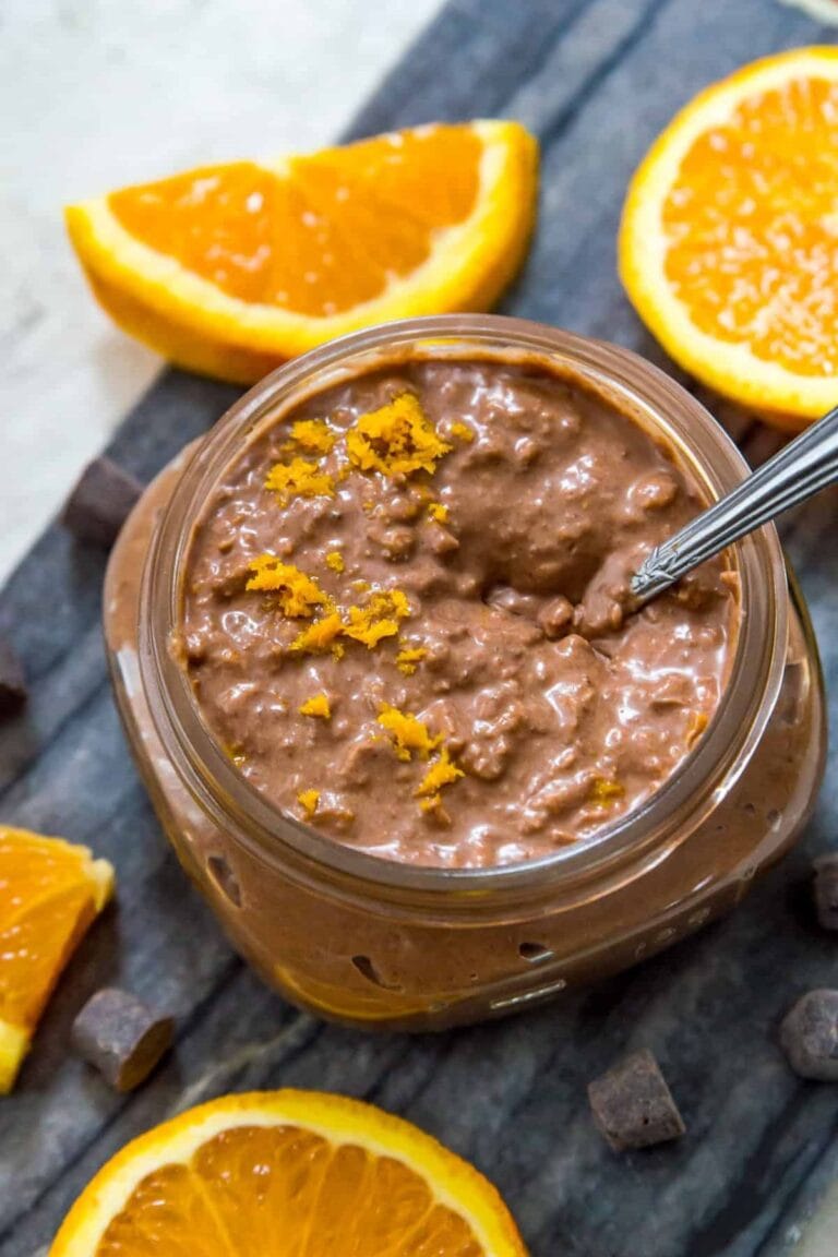 Jar of chocolate orange overnight oats surrounded by orange slices and bits of chocolate.