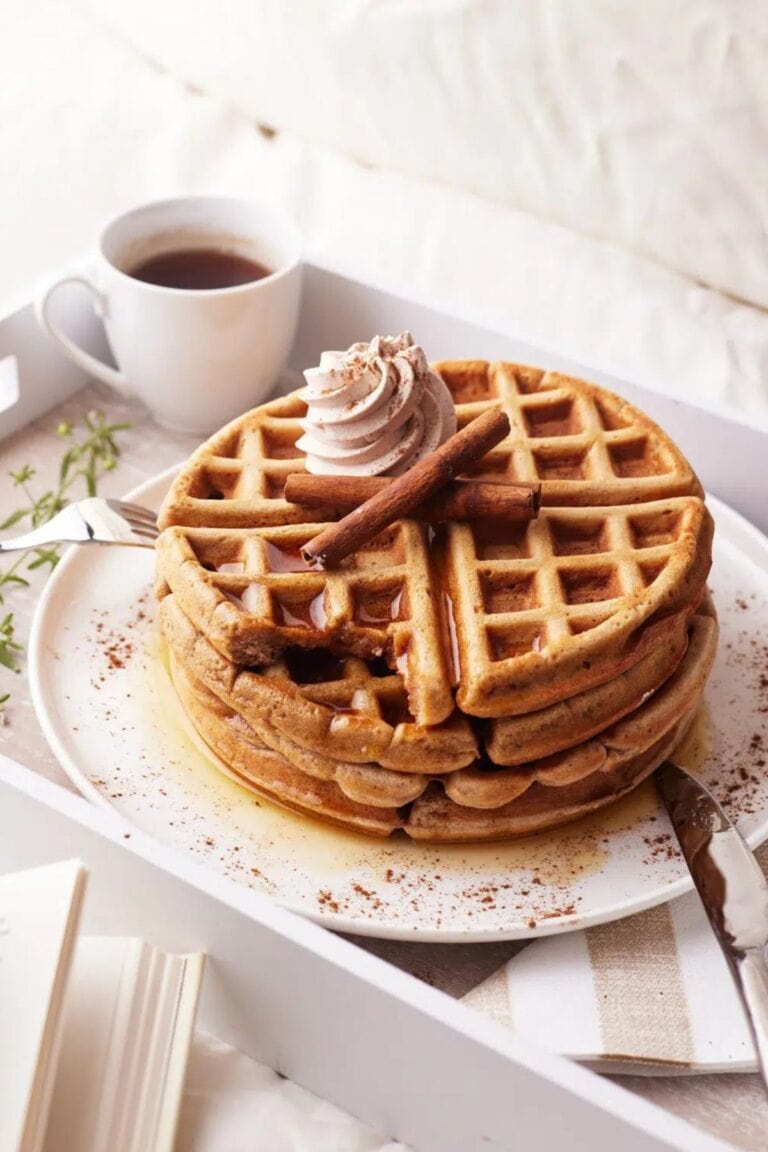 Stack of cinnamon waffles on a plate set on a breakfast tray with a cup of coffee.