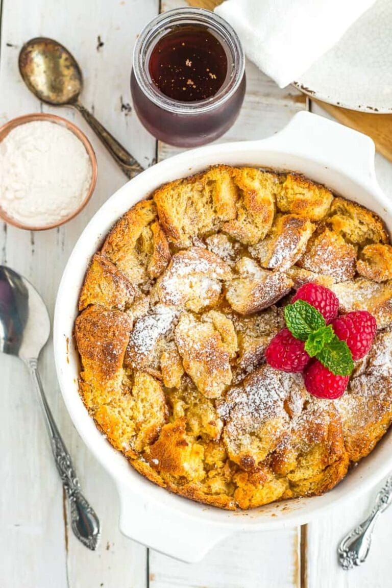 Eggnog bread pudding in a white baking dish garnished with a few raspberries and a sprig of mint.