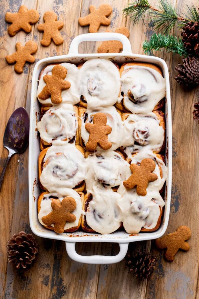 White baking dish full of gingerbread cinnamon rolls topped with frosting and a few small gingerbread men.