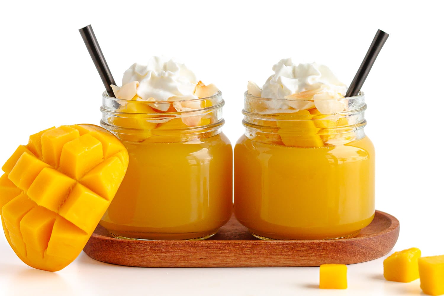 Two mango jellies in small glass jars topped with fresh diced mango, toasted coconut flakes and whipped cream.