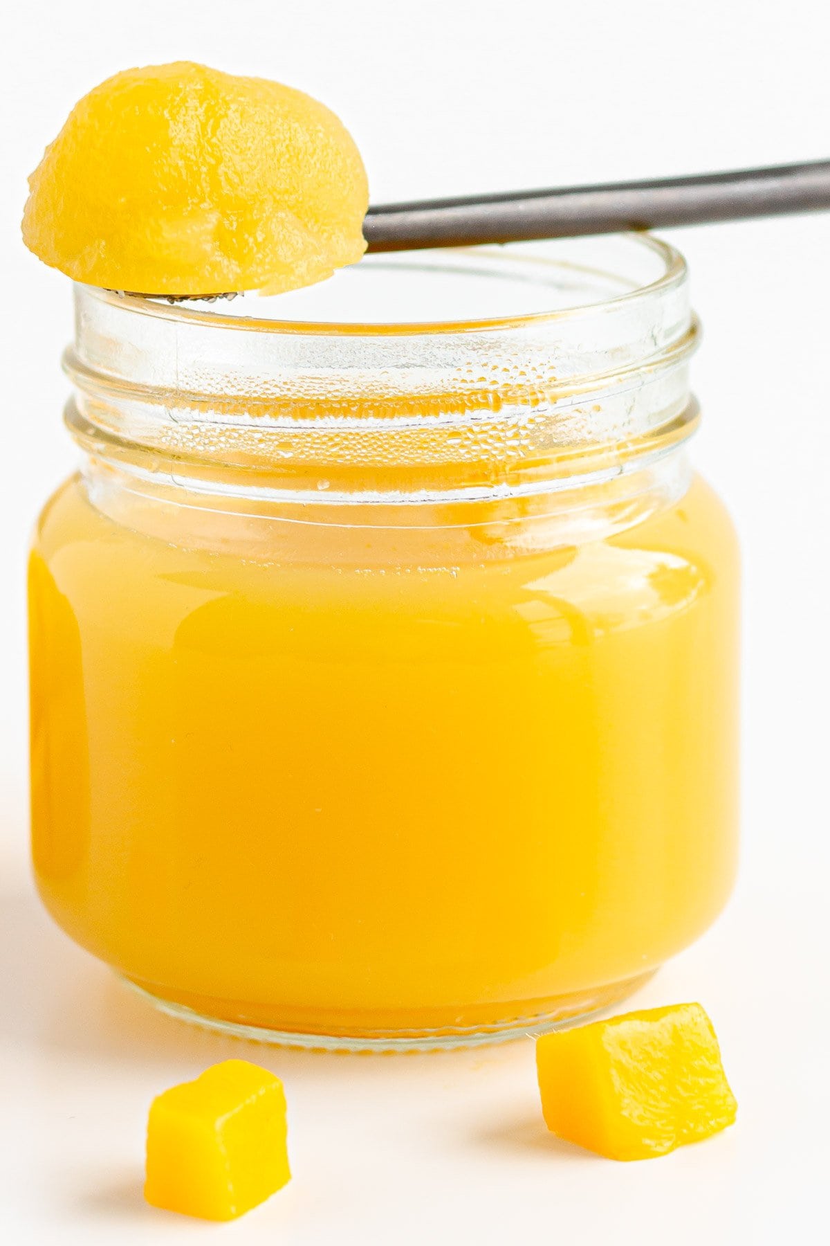 Jar of mango jelly with spoonful resting on top.