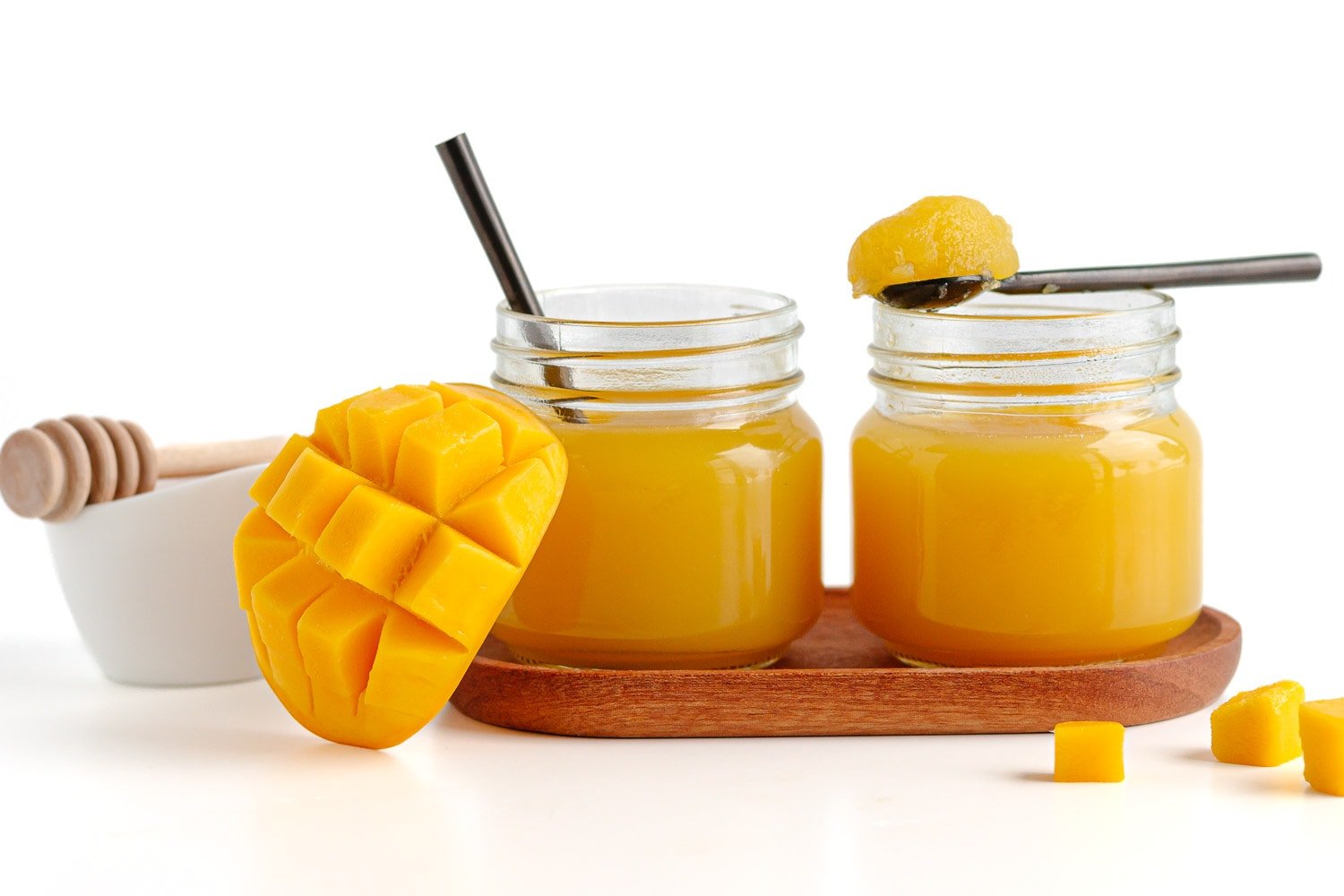 Homemade mango jello in 2 glass jars next to some sliced fresh mango and a small honey bowl.