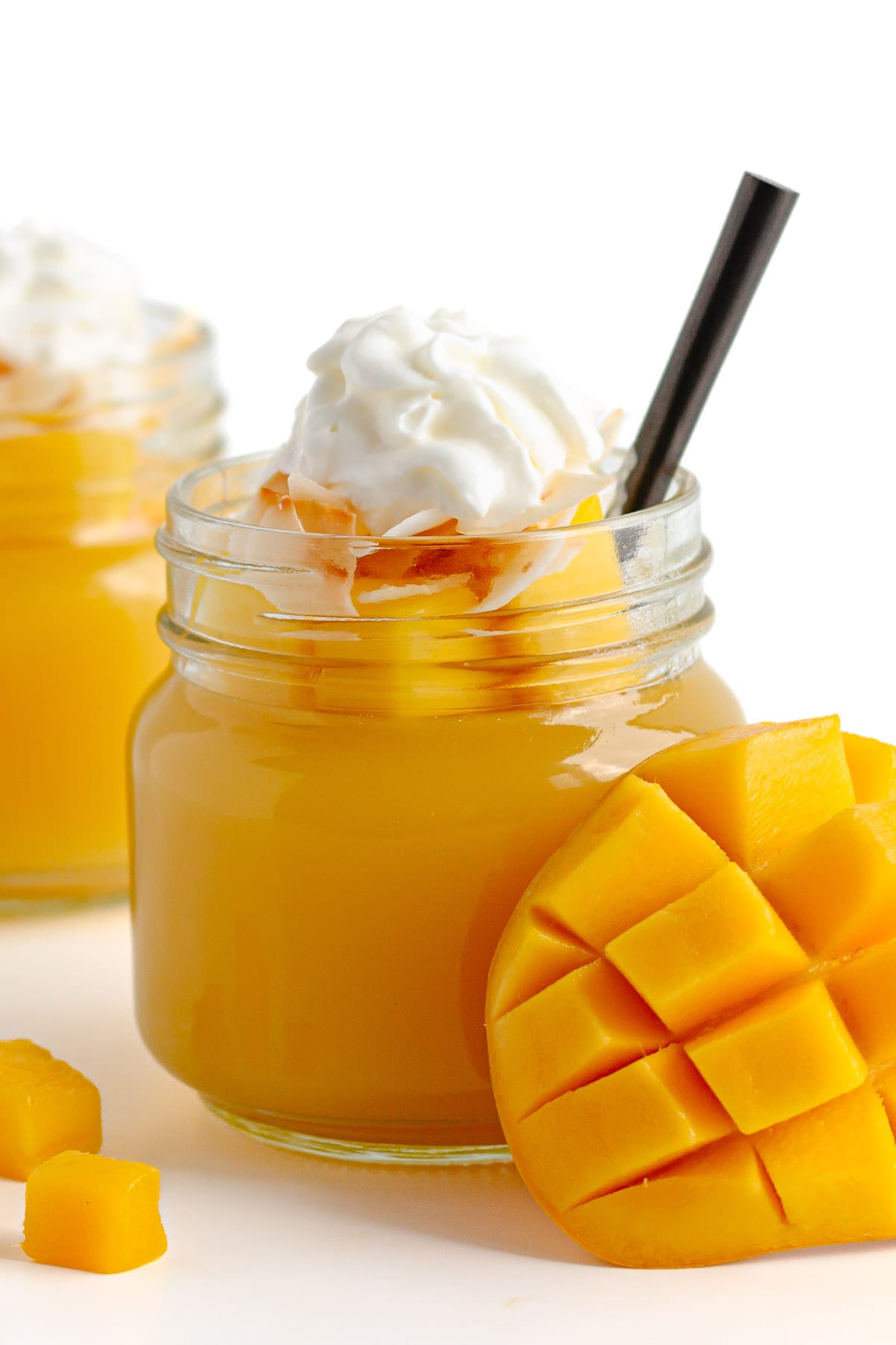 Jar of mango jelly topped with diced mango, coconut flakes and whipped cream.