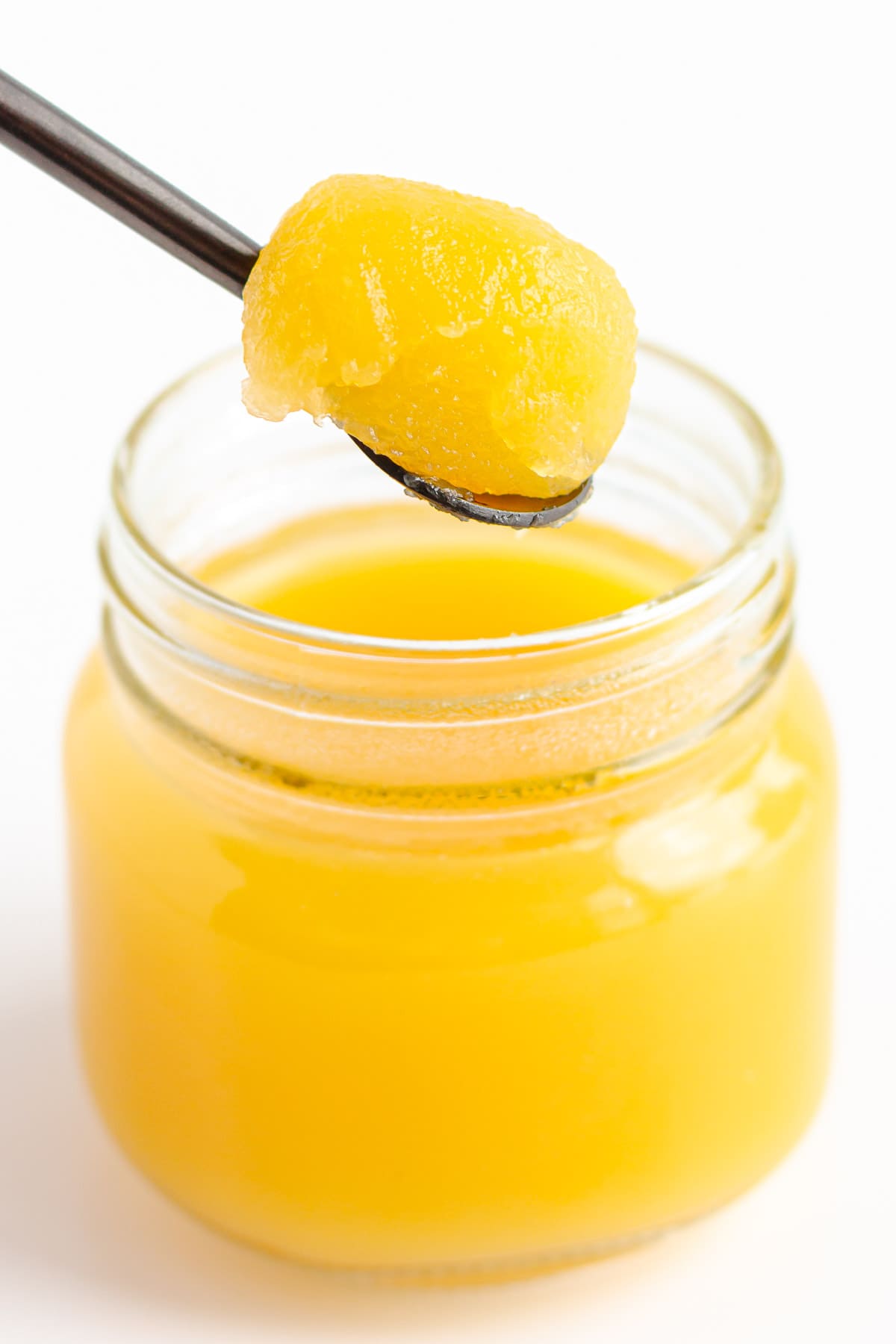 Fully set mango jelly being scooped out of small glass jar with a spoon.