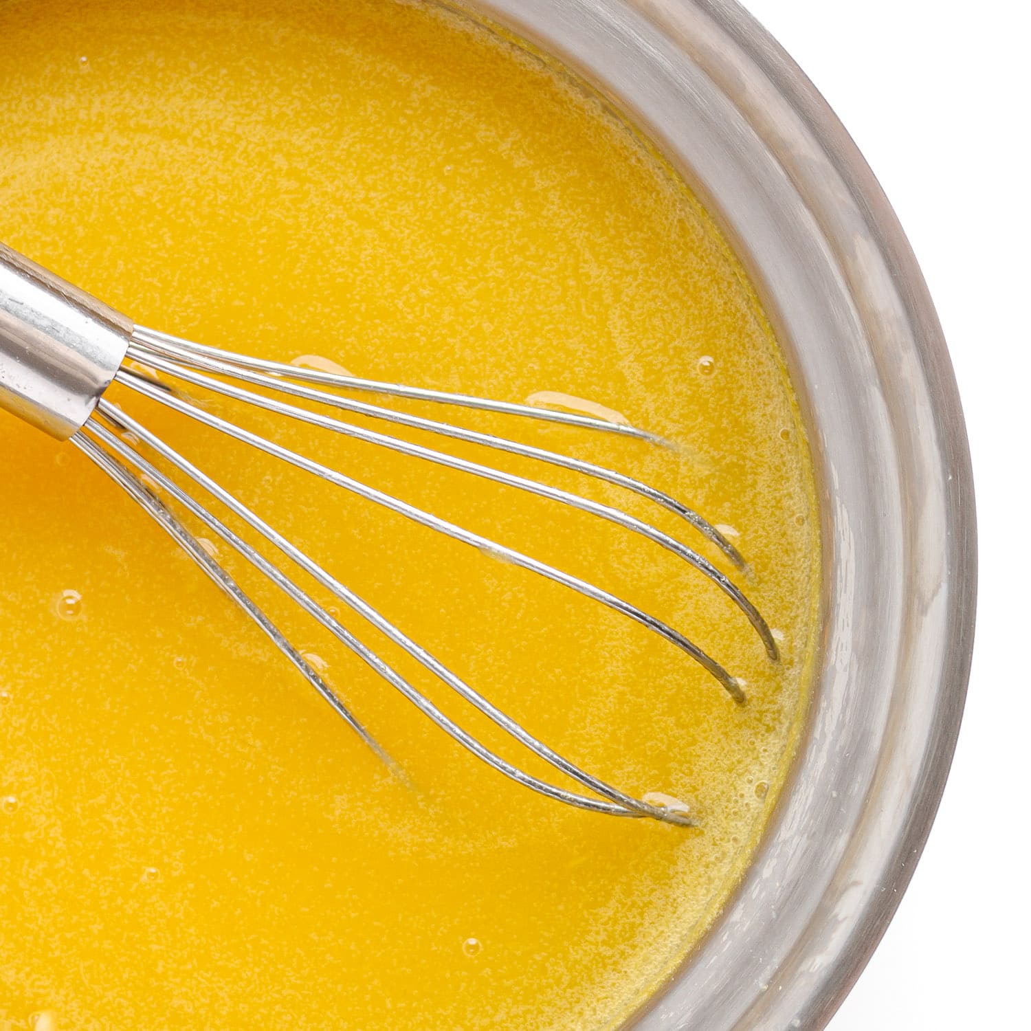 Softened gelatin being whisked into mango mixture in a saucepan.