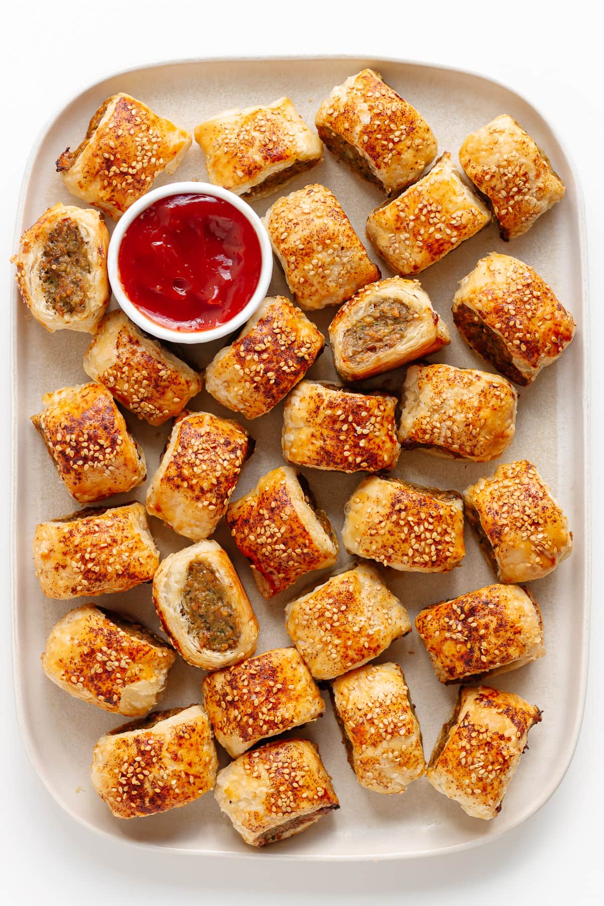 Rectangular platter of chicken sausage rolls with a small bowl of ketchup for dipping.