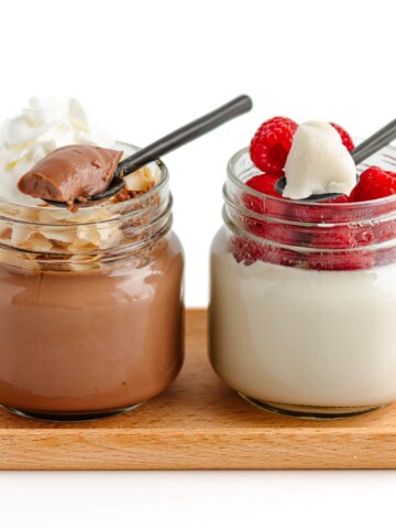 Two glass jars of coconut jelly with spoons scooping some out, one chocolate flavored and one vanilla flavored.