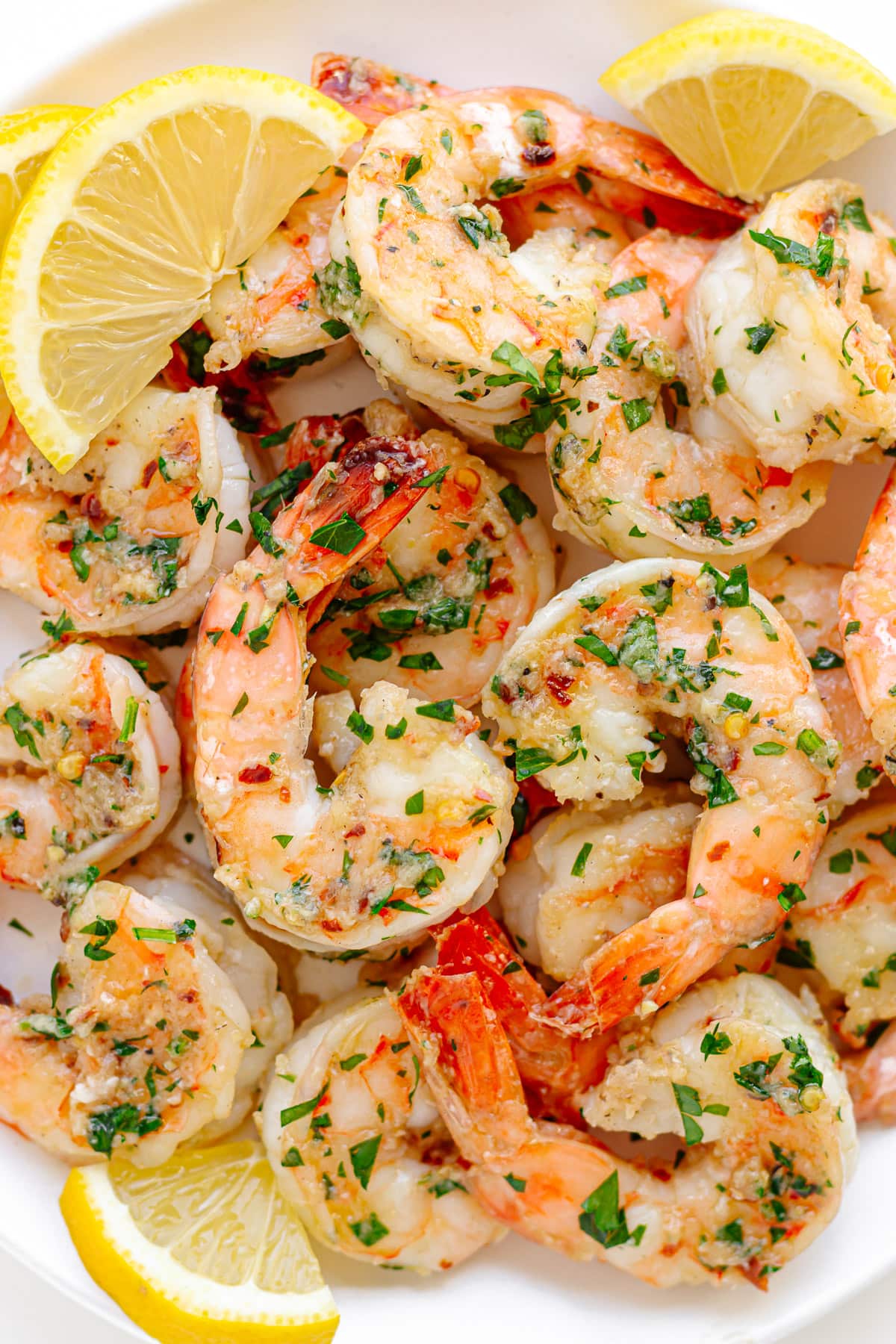 Garlic ginger sautéed shrimp on a white serving dish garnished with lemon slices and chopped parsley. 