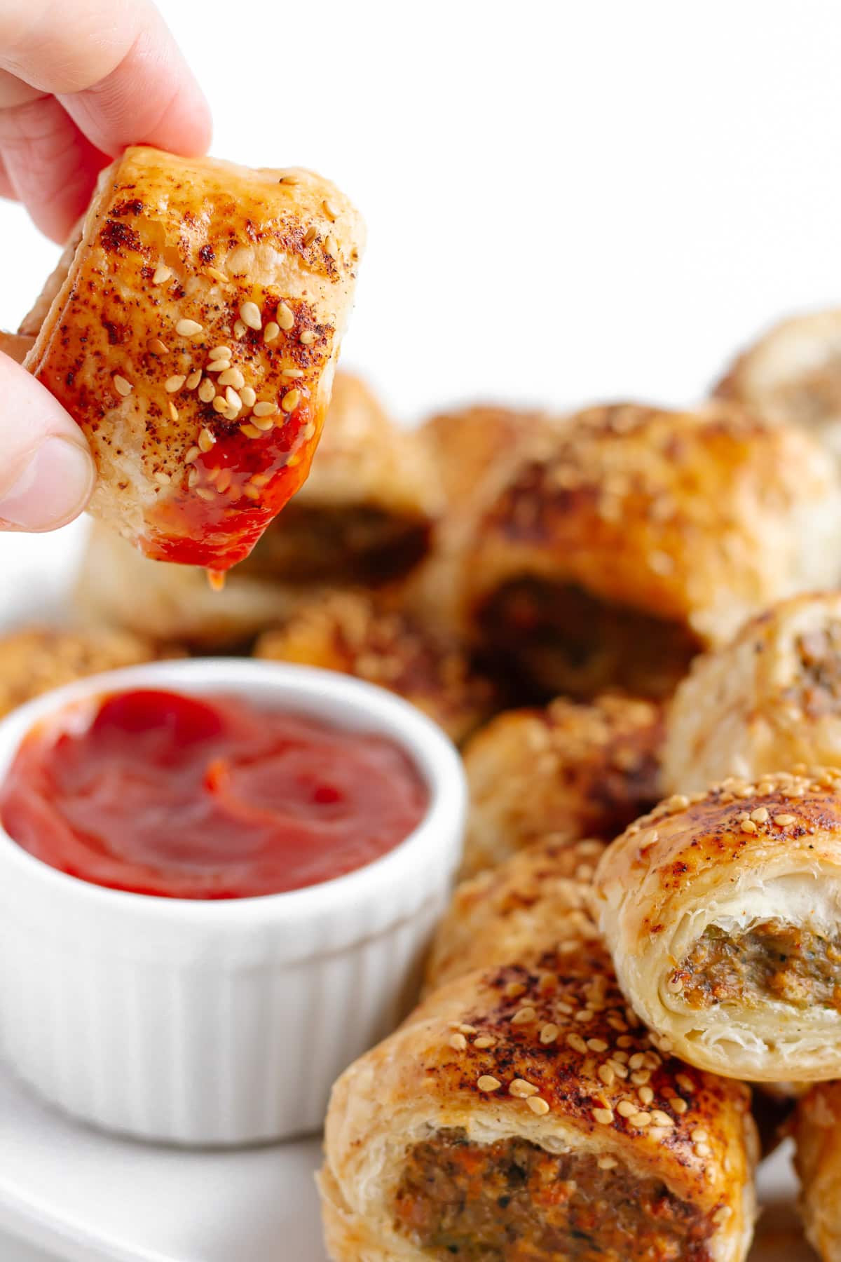 Hand dipping a chicken sausage roll in bowl of ketchup.