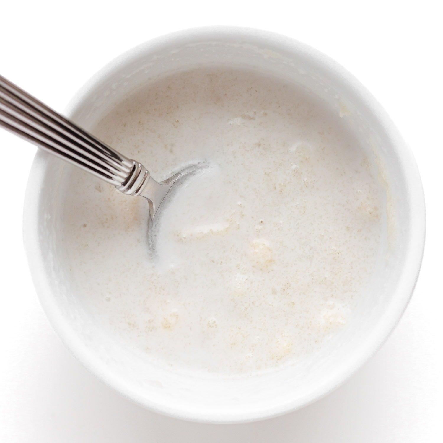 Hydrating gelatin powder in a small white bowl of coconut milk.