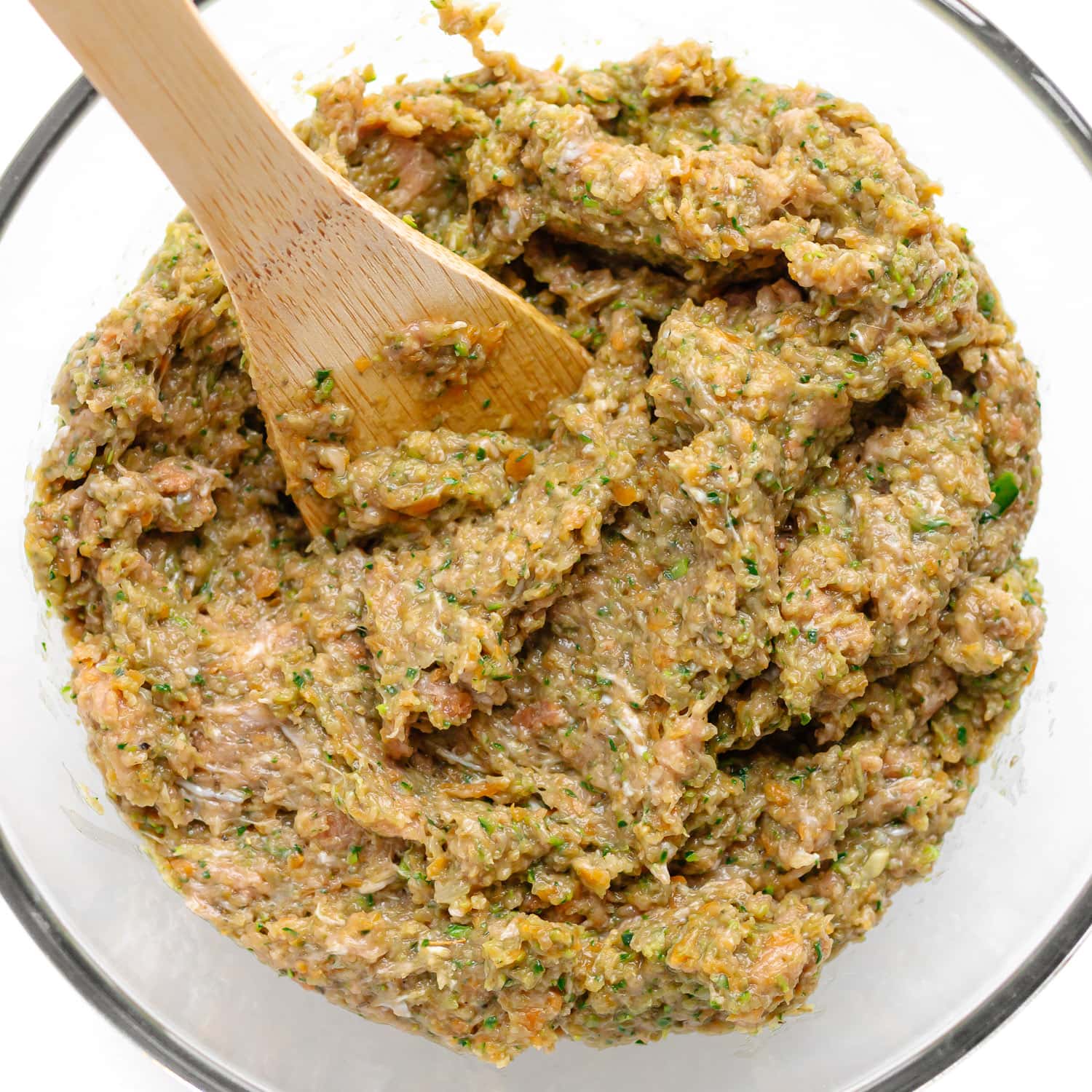 Filling for chicken sausage rolls being mixed together in a glass bowl.