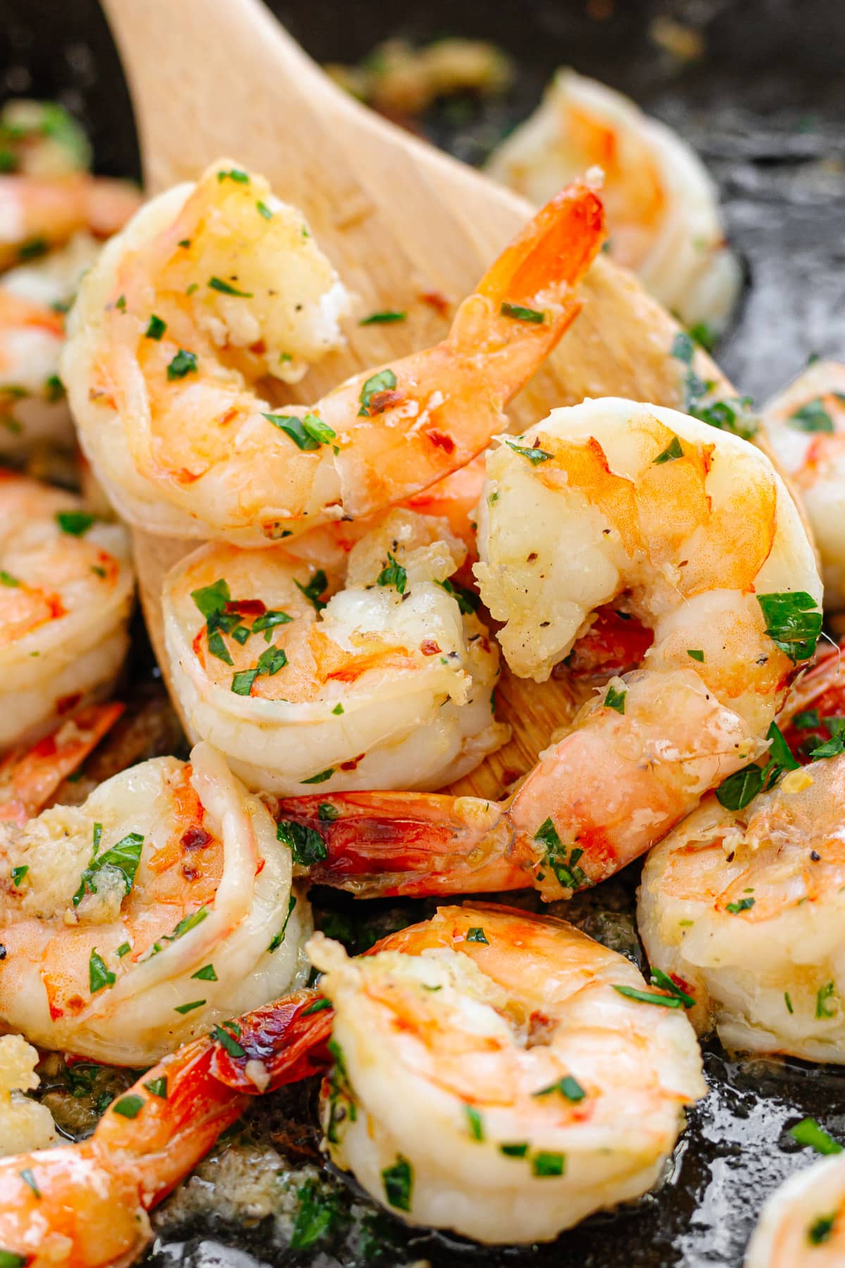 Pan fried shrimp in a cast iron skillet being picked up with a wooden spatula.