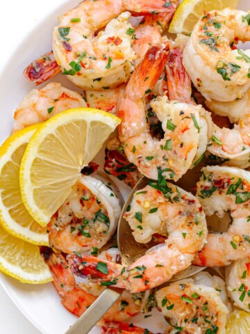 Garlic ginger pan seared shrimp on a white serving plate garnished with lemon slices and chopped parsley.