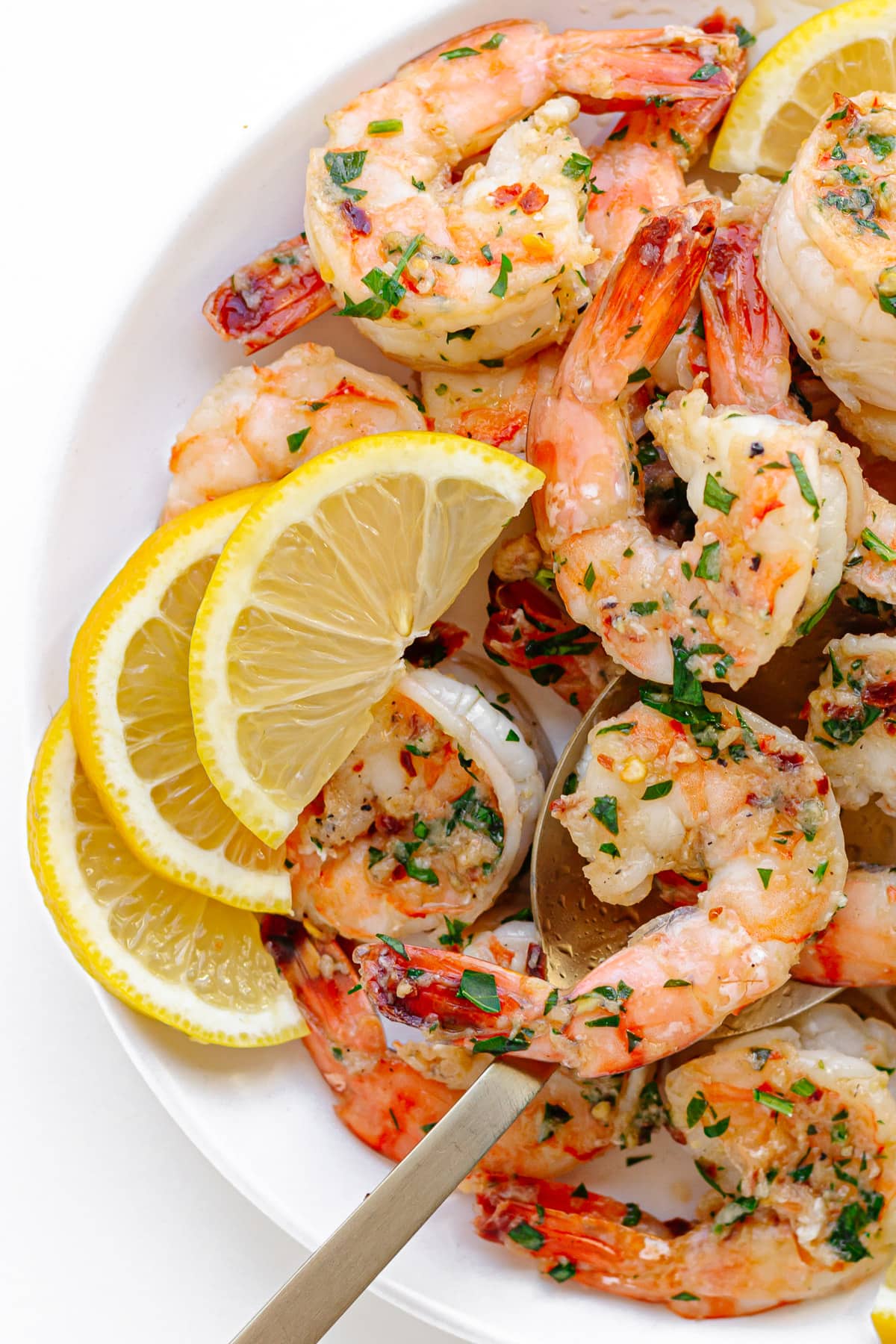 Pan seared shrimp on a white serving plate garnished with lemon slices and chopped parsley.