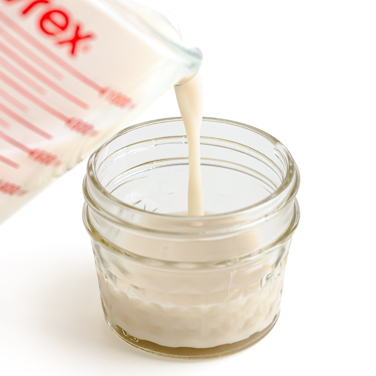 Coconut jelly mixture being poured from a glass measuring cup into a small glass jar.