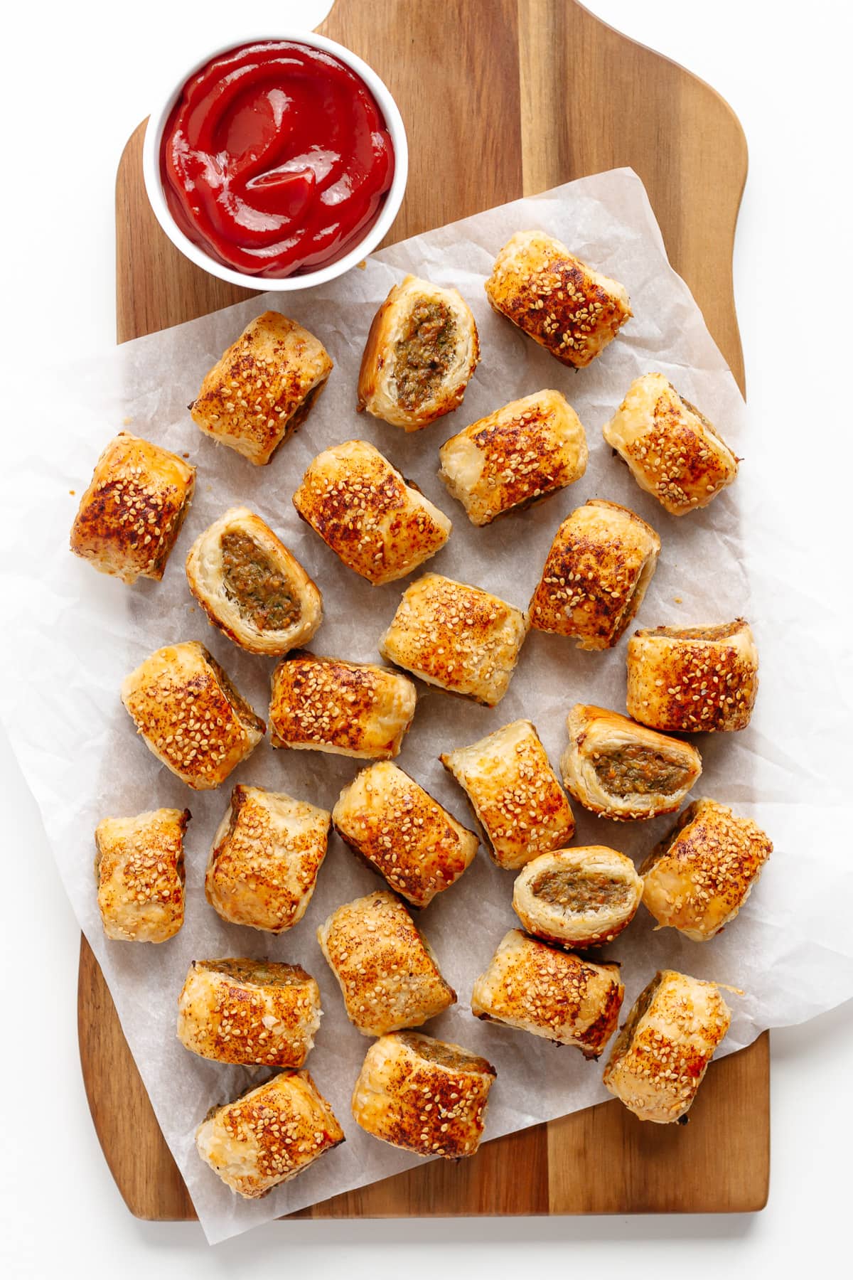 Puff pastry sausage rolls on a wooden serving board with bowl of ketchup.