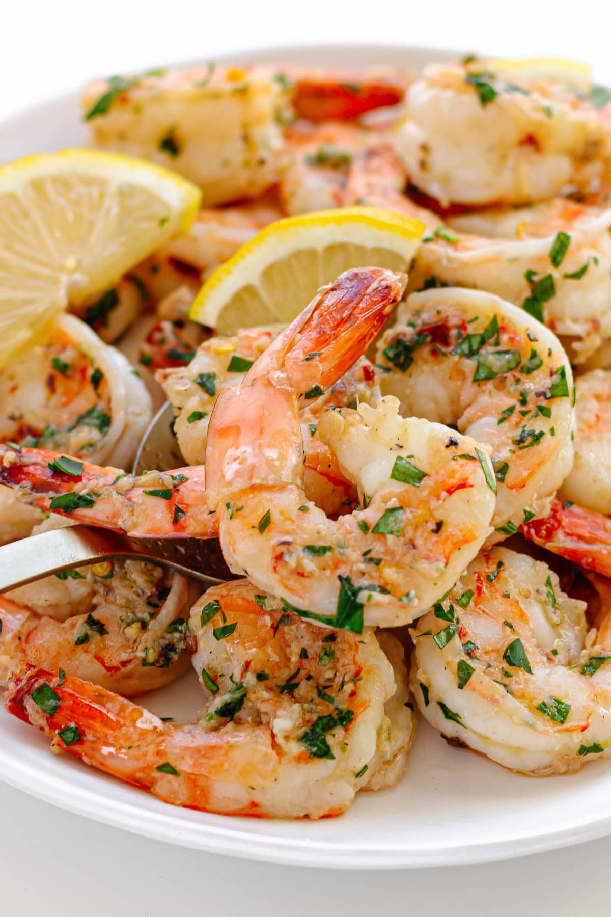 Garlic ginger sautéed shrimp on a white serving plate with serving spoon. 