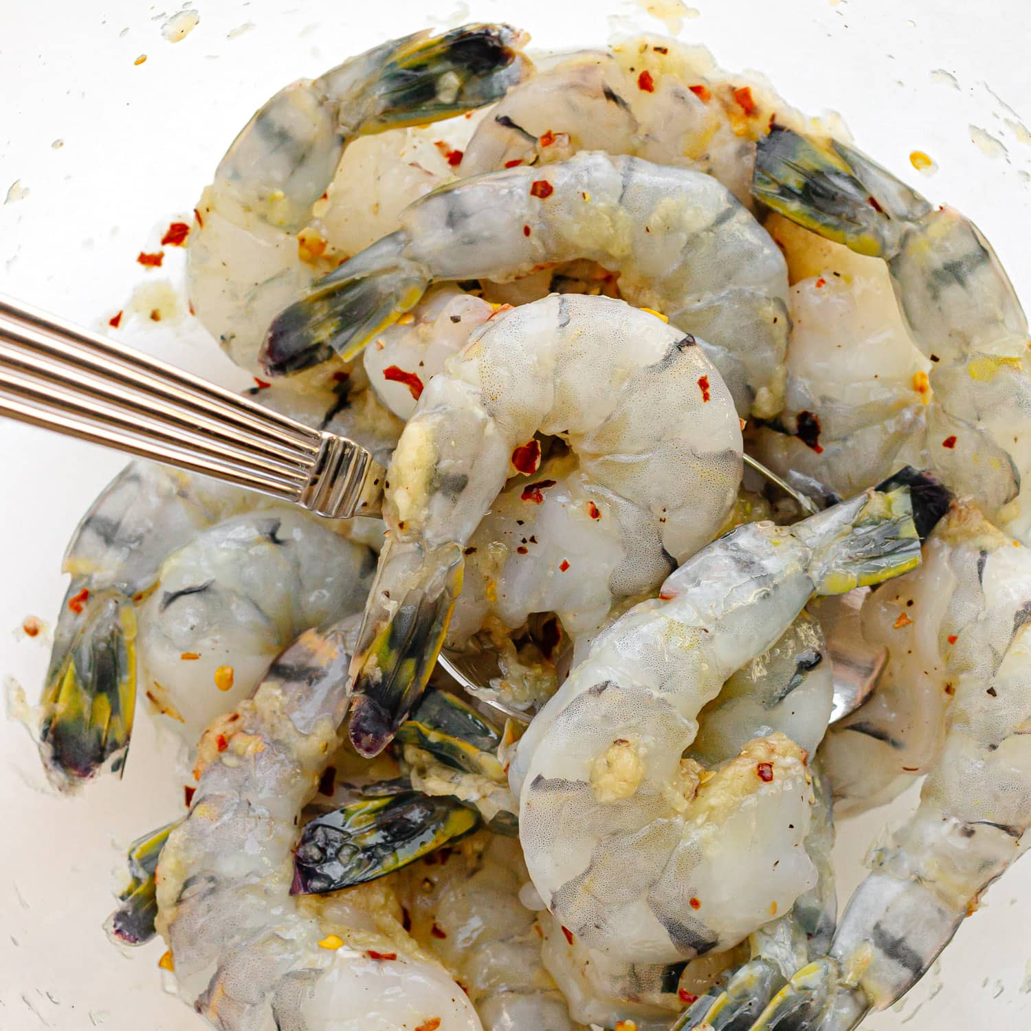 Raw shrimp being mixed together with garlic, ginger, red pepper flakes, salt and pepper.