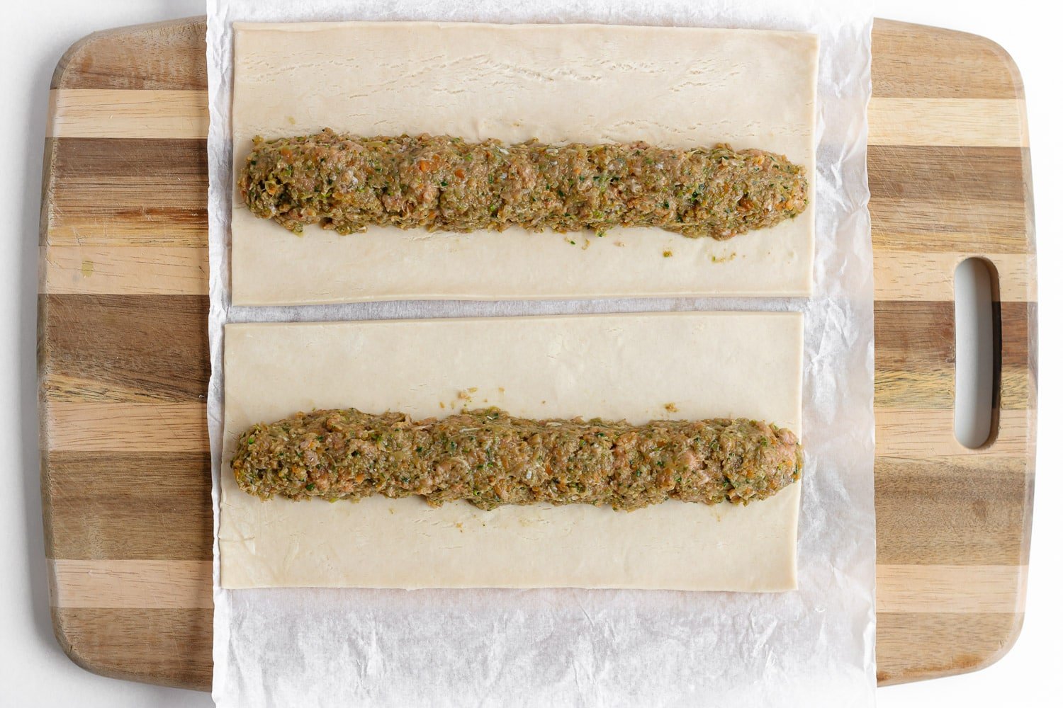 Shaping sausage roll filling into a log shape down the center of puff pastry.