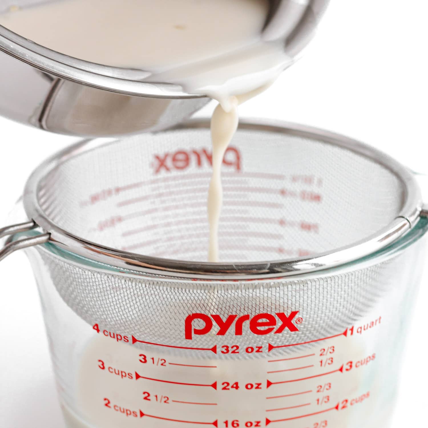 Pouring coconut jelly mixture from saucepan into a fine mesh sieve set over a large glass measuring cup.